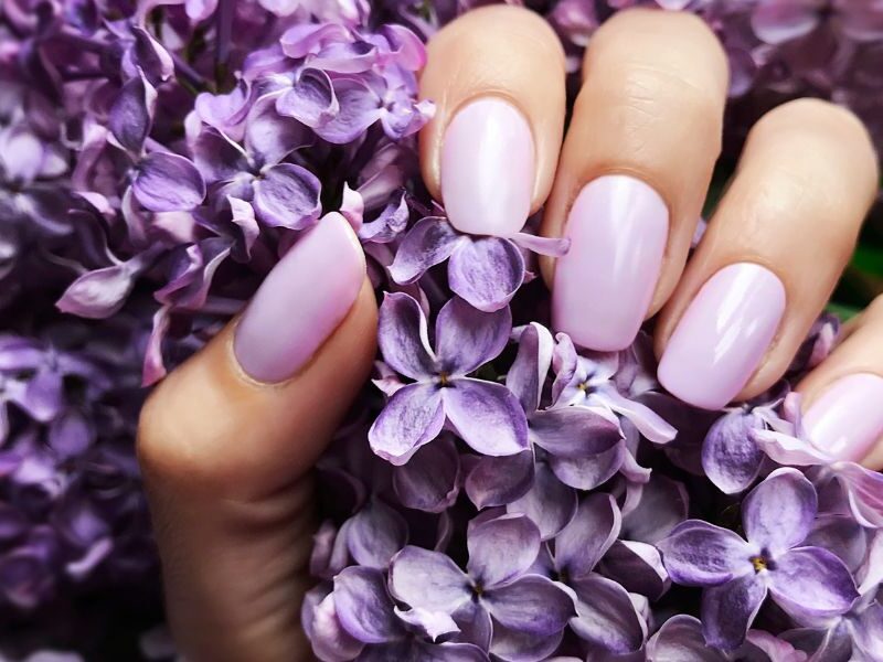 Uñas lavanda pastel con acabado brillante, mano sosteniendo flores lila